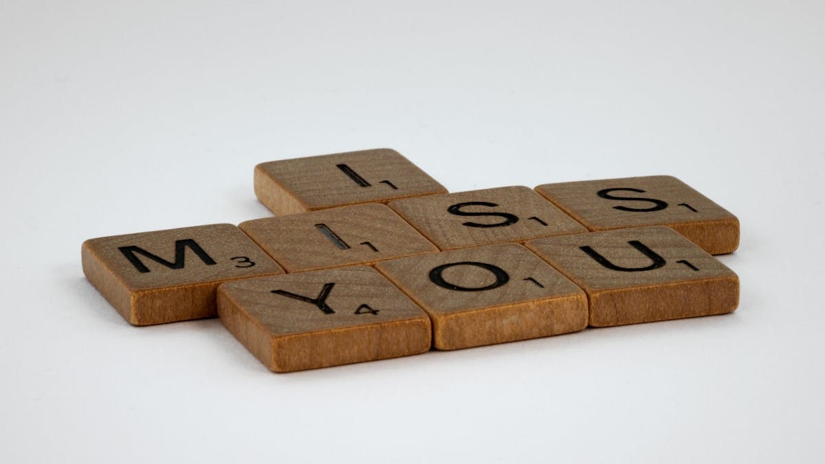 Close-up of Scrabble tiles spelling 'I Miss You' on a white surface with ample copy space.