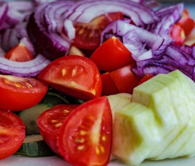 Colorful summer vegetable salad featuring tomatoes, cucumbers, and red onion slices on a plate.